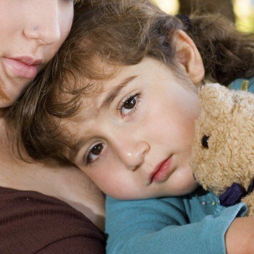 ein Mädchen hält einen Teddybären vor sich an die Brust und lehnt sich an ihre Mutter an