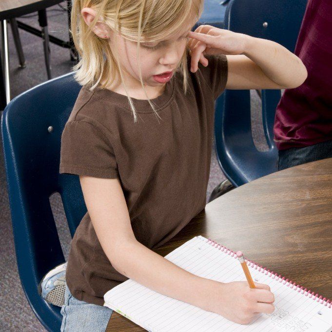 ein Kind sitzt vor einem runden Holztisch und schreibt mit der rechten Hand auf einen Block
