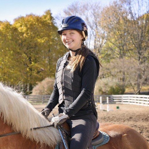 ein Mädchen in Reitkleidung sitzt auf einem Pferd und reitet auf einem Reitplatz