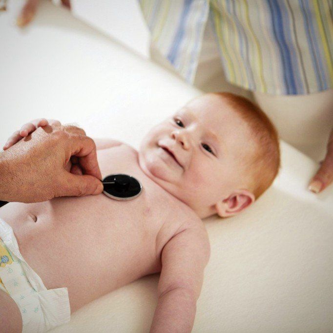 ein Säugling liegt auf einer weißen Unterlage und wird mit einem Stethoskop an der Brust abgehört