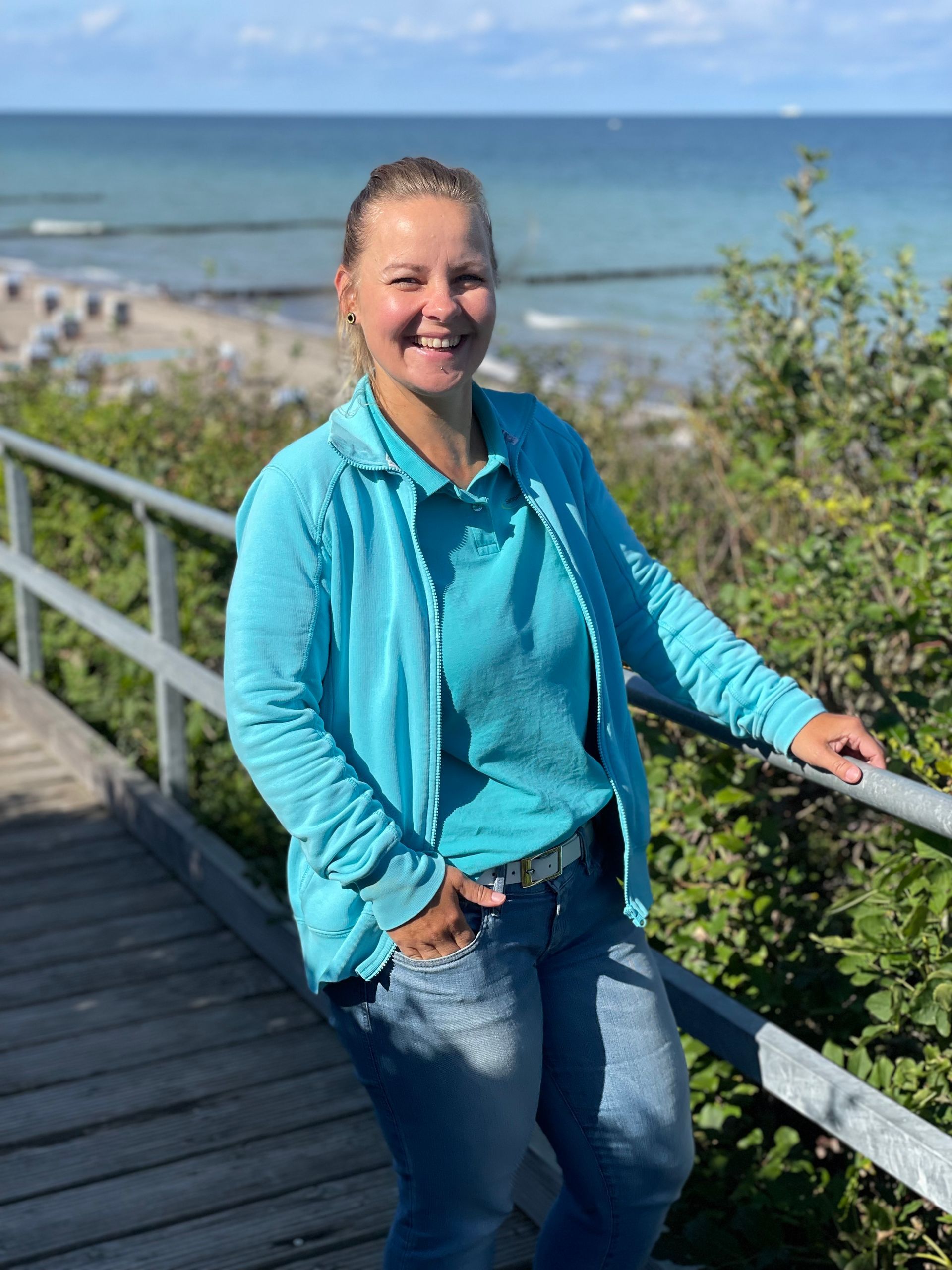 Blonde Frau, die Pflegedienstleiterin des ambulanten Pflegedienst in Rostock Lütten Klein und der Tagespflege. Im Hintergrund ist die Ostsee zu sehen.