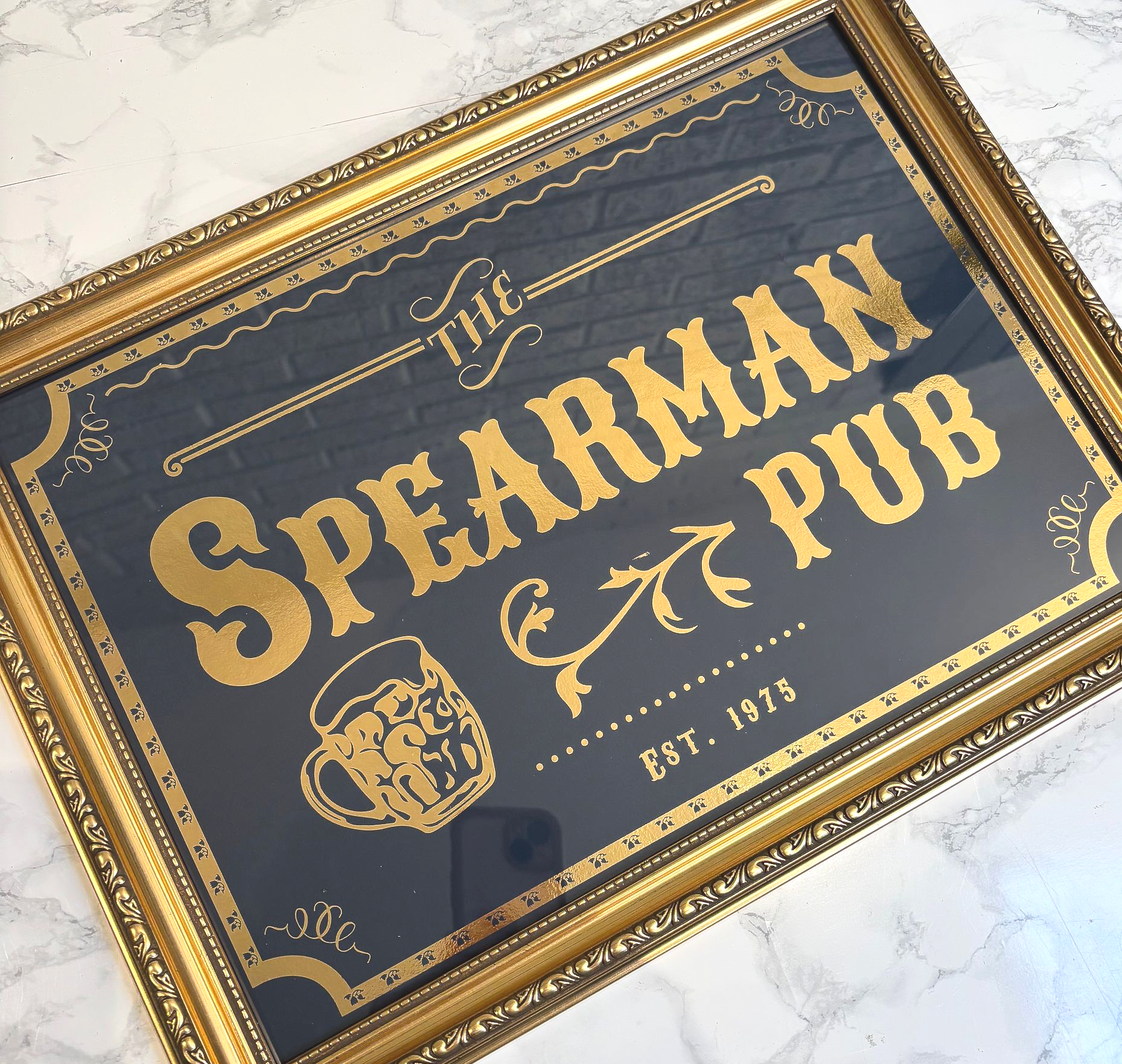 Gold foil pub sign with custom text ‘The Anderson Arms’, featuring vintage typography and beer mug design in gold frame.