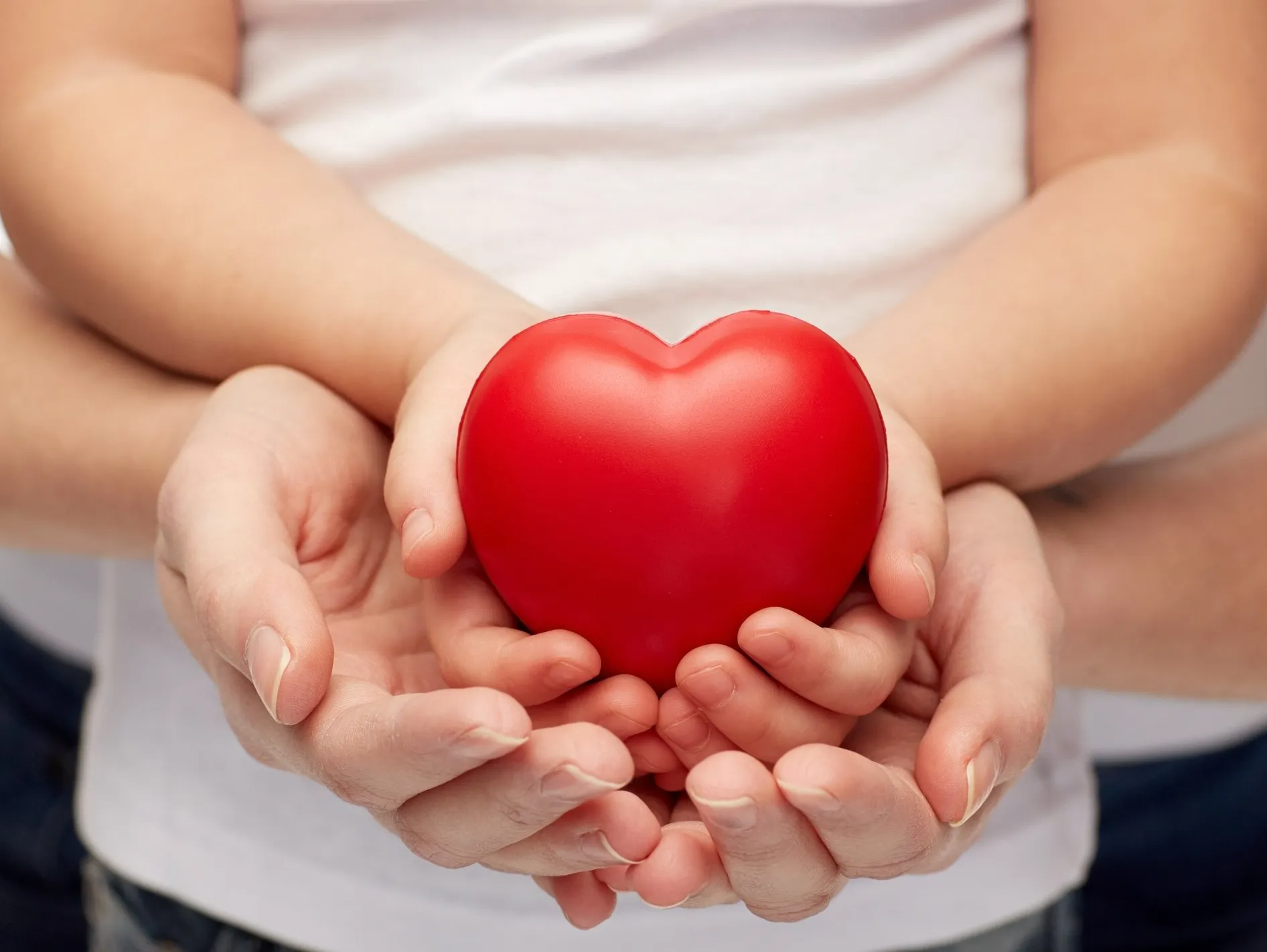 Gebende Hände eines Kindes liegen in gebenden Händen einer Frau. Das Kind hält ein rotes Herz in den Händen.