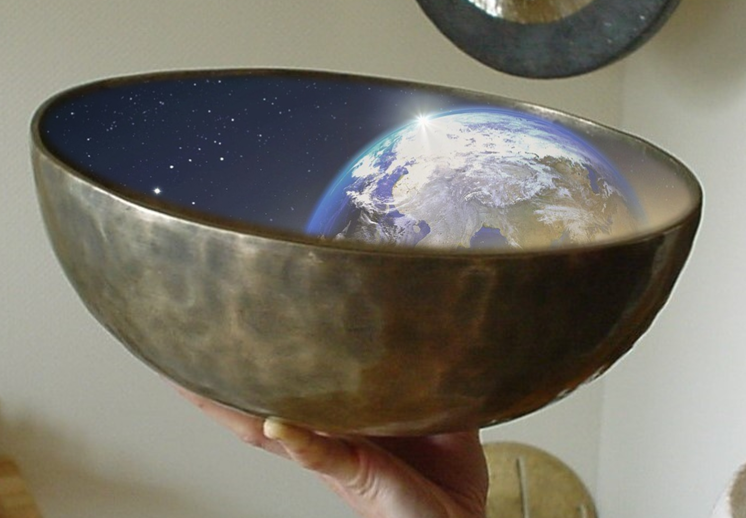 Eine Hand hält eine Klangschale und in der Klangschale liegt eine Weltenkugel.