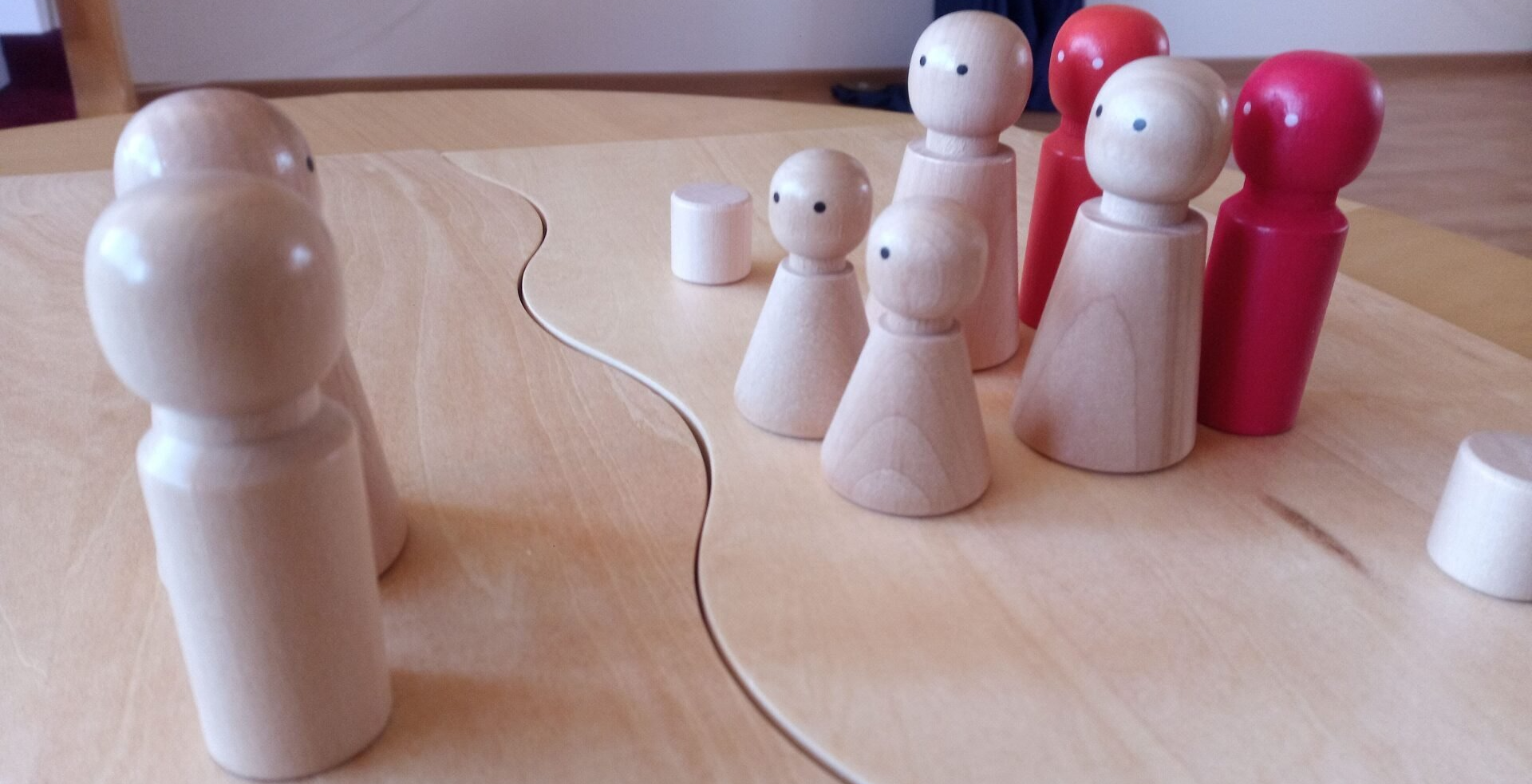 6 Holzfiguren stehen auf einem Brett 2 weiteren Holzfiguren gegenüber und sind Stellvertreter für Familienangehörige.