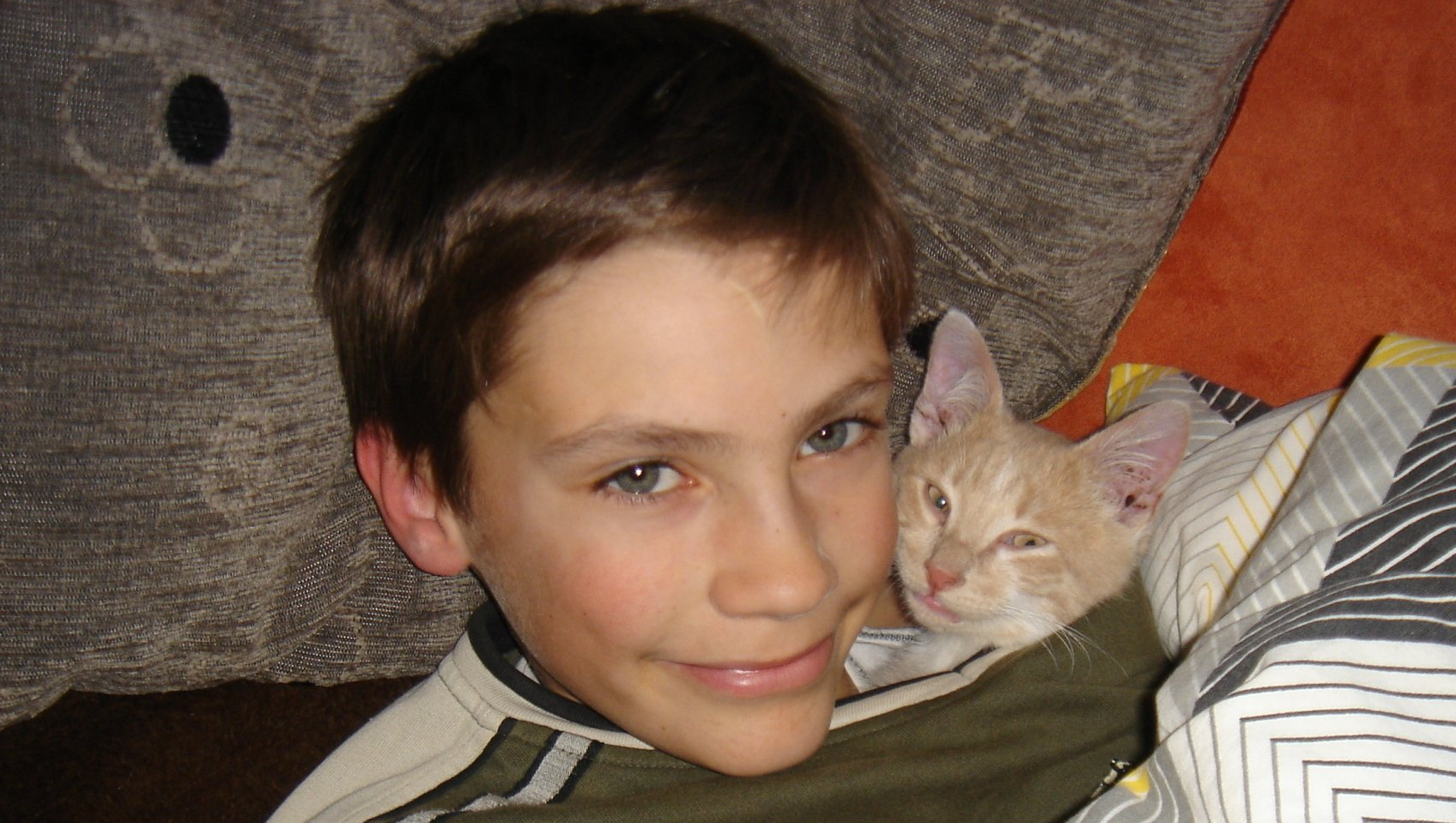 Ein Junge mit einer Katze. Er schaut ganz verträumt und hat seinen Kopf an den Katzenkopf geschmiegt.