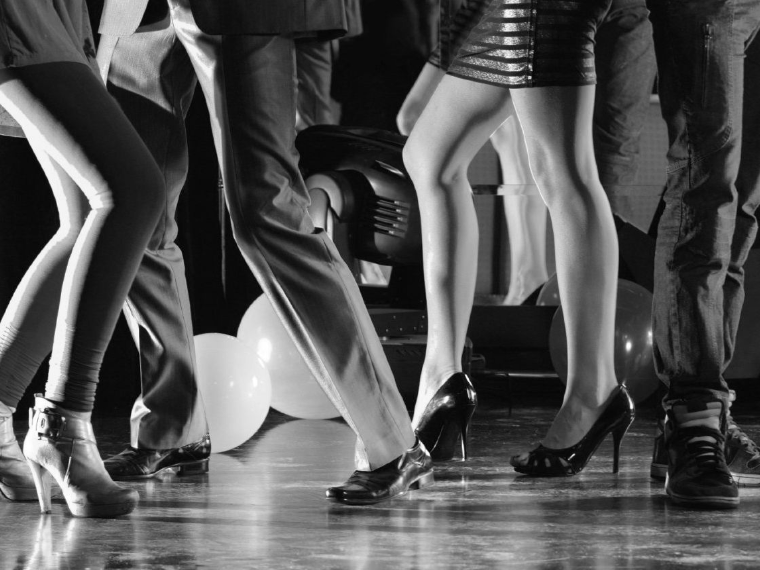EVENT DJ - Men and women dancing at a dance party shown from the waste down with colorful party lighting and balloons around them.