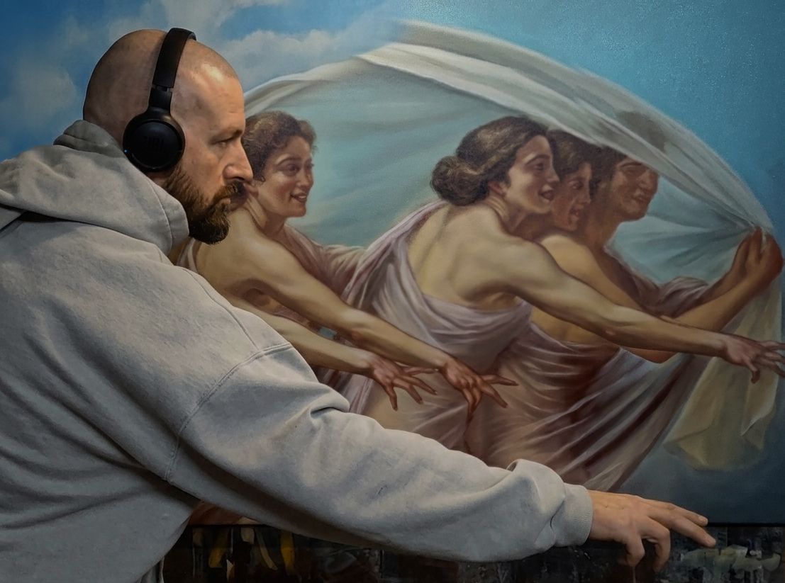 Ein realistisches Oelgemaelde des Frankfurter Kuenstlers Drew Camell, das eine Gruppe von Frauenfiguren im Stil der Alten Meister darstellt. Die Figuren sind mit weichen, fließenden Tuechern bedeckt und strecken ihre Haende nach vorne, waehrend ein Mann, Drew Camell mit Kopfhoerern und einem grauen Kapuzenpullover im Vordergrund steht und das Gemaelde nachamt. Die Komposition verbindet klassische Maltechniken mit einem modernen Kontext. Beeindruckend ist die Transparenz der gemalten Stoffe in dem Bild.