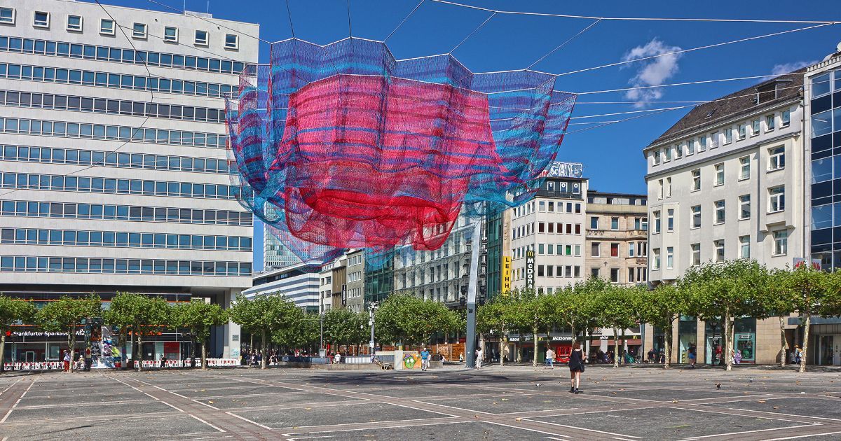 Farbenprächtige Netzskulptur von Janet Echelman in Magenta und Blau, die an
Spannseilen frei über de