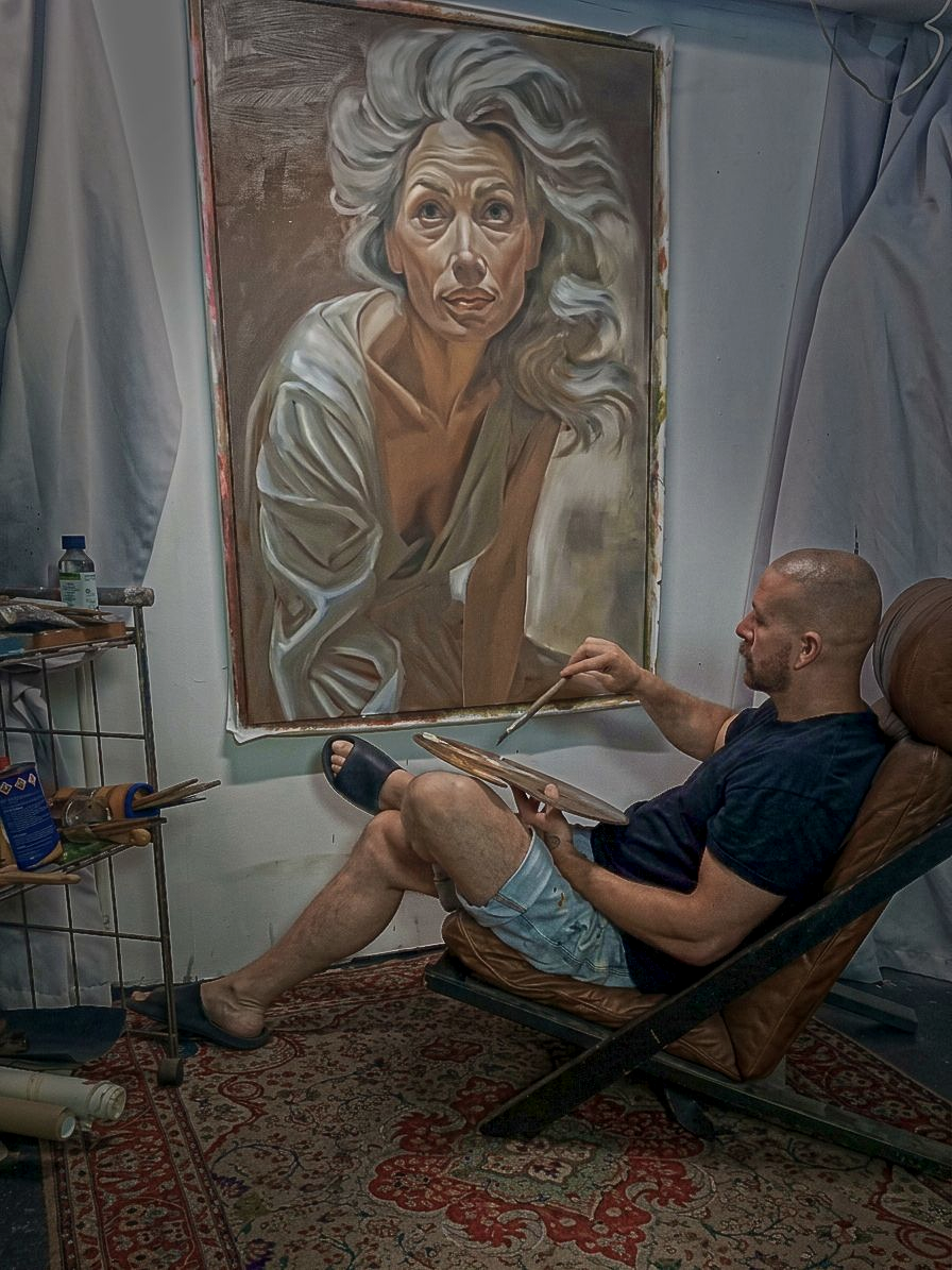 Der Frankfurter Bildende Kuenstler und Kunstmaler in seinem Atelier in Frankfurt Hoechst. Er sitzt zwischen Oelfarben auf einem Designersessel und malt an einem Portraet Kunstwerk mit Oelfarben.