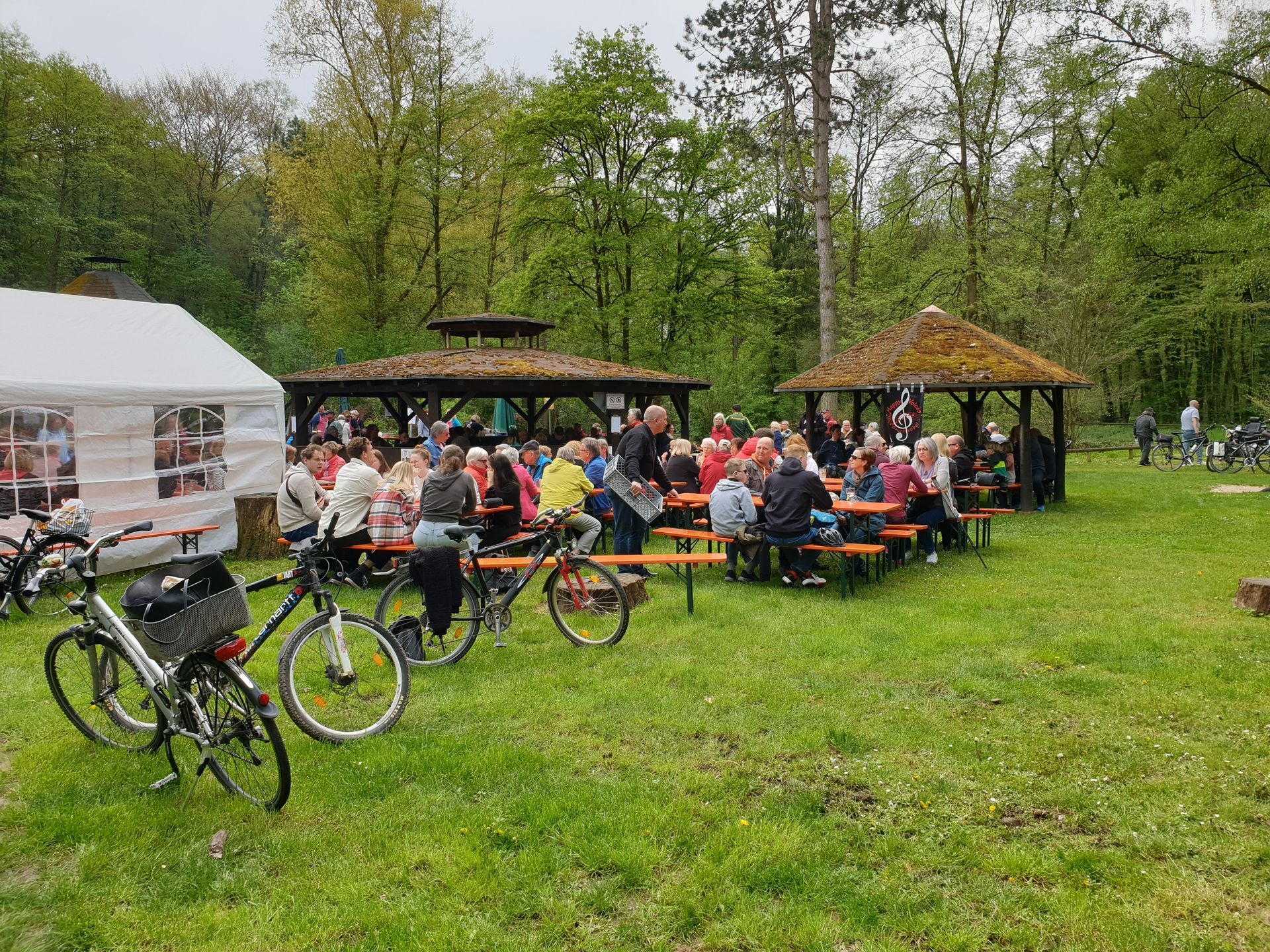 Zahlreiche Gäste sitzen auf Bierbänken im Wald an der Dicken Eiche.