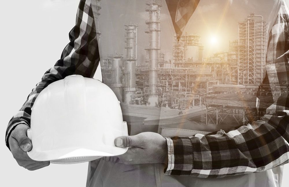 Bauarbeiter hält Helm in der Hand, im Hintergrund ist Industrie Gebäude