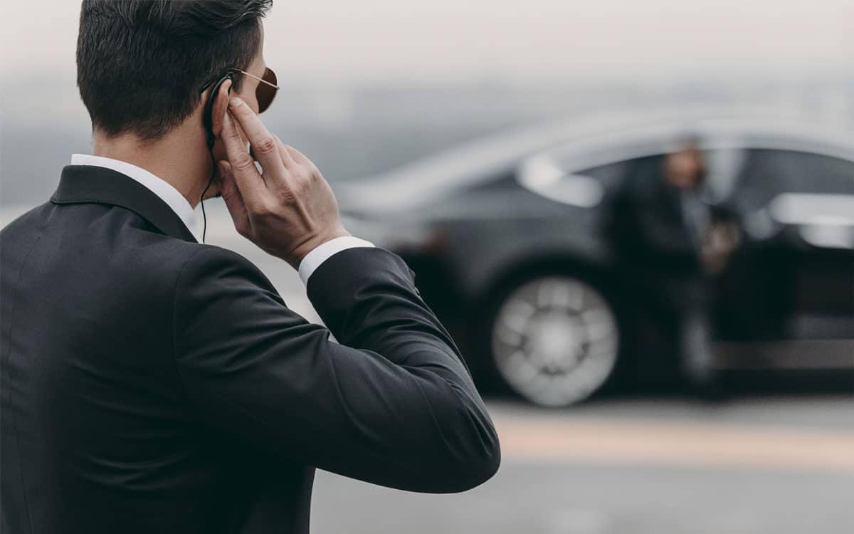 bodyguard in. suit opening a door of a nice car for the client