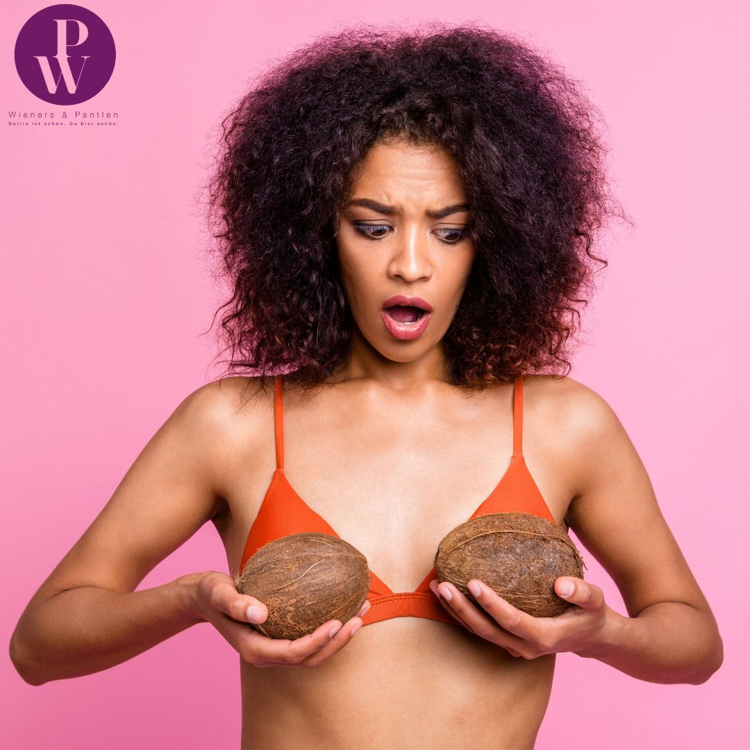 Dunkelhäutige Frau hält sich Kokosnüsse vor die Brust zum Testen der neuen Brustgröße
