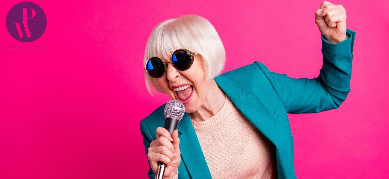 Ältere Frau mit Sonnenbrille und grauem Haar singt in Mikrofon und posiert
