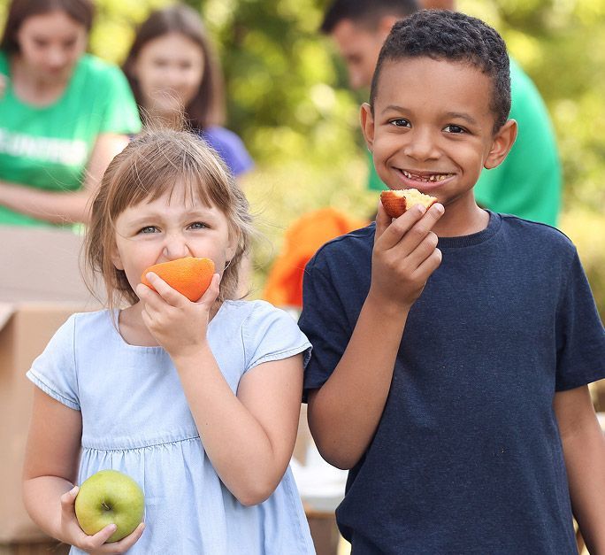 Two kids eating fruits at a food distribution event.