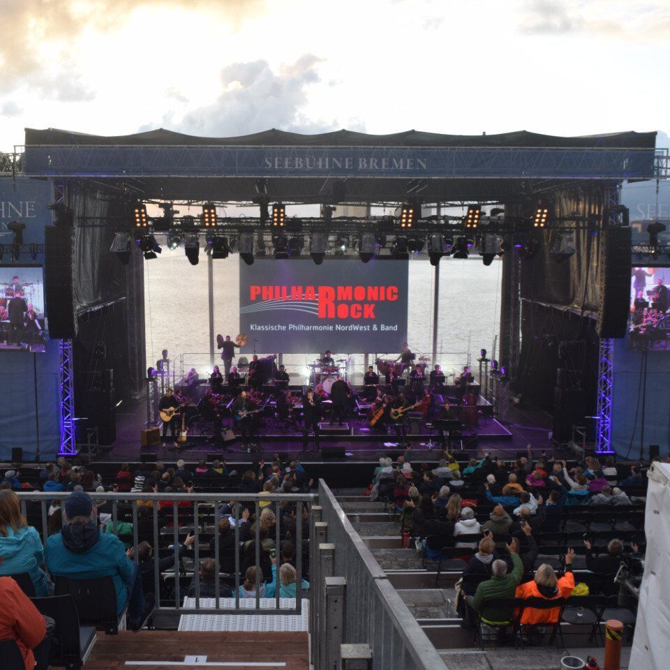 Konzert Seebühne Bremen Die Band und das Orchester von Philharmonic Rock spielen ein Konzert auf einer Open-Air-Bühne.