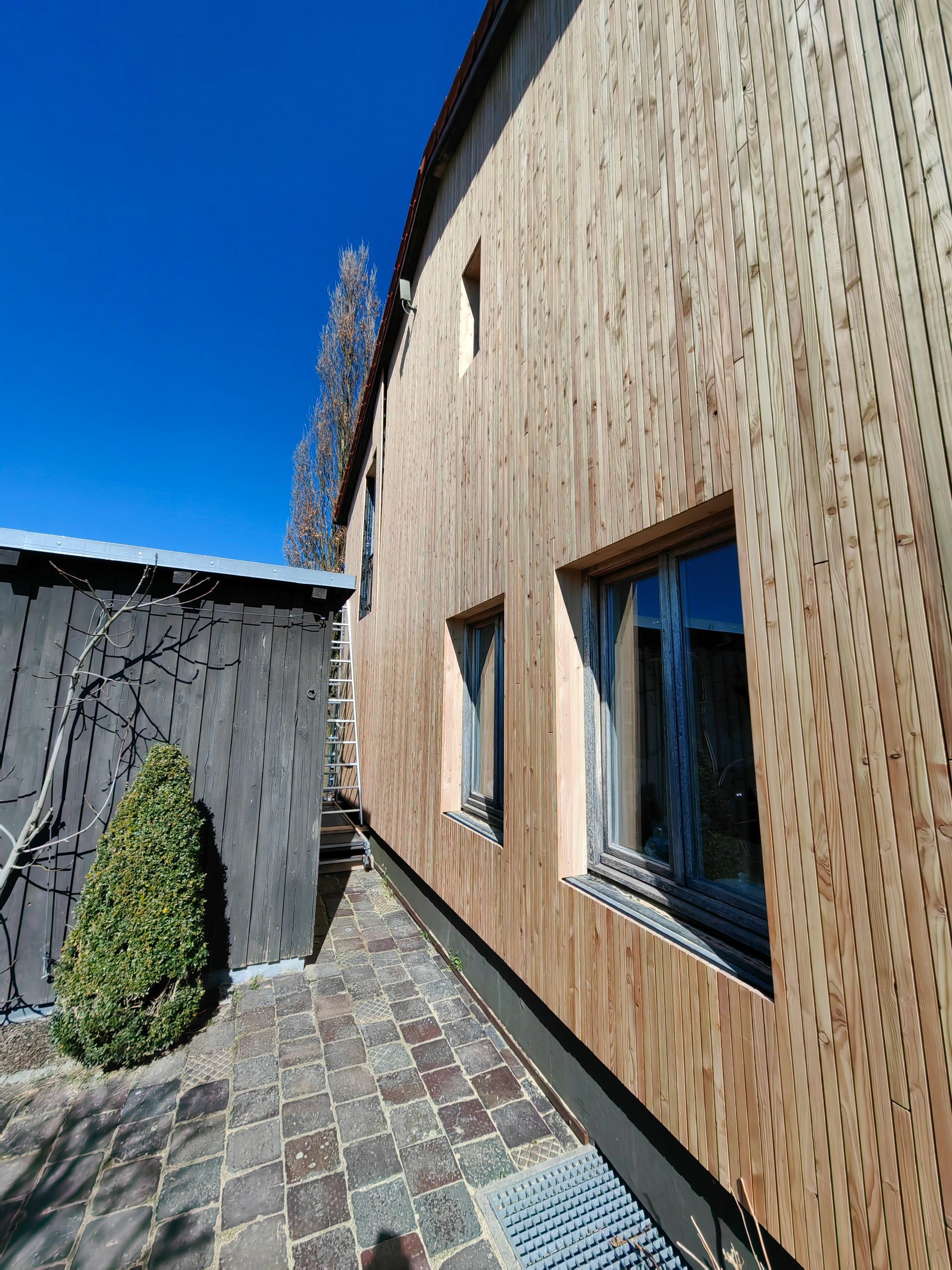 Seitliche Ansicht einer erneuerten Holzfassade mit strukturierter Oberfläche - natürliche Ausstrahlung durch unbehandelte Lärchenbretter im Raum Chiemgau