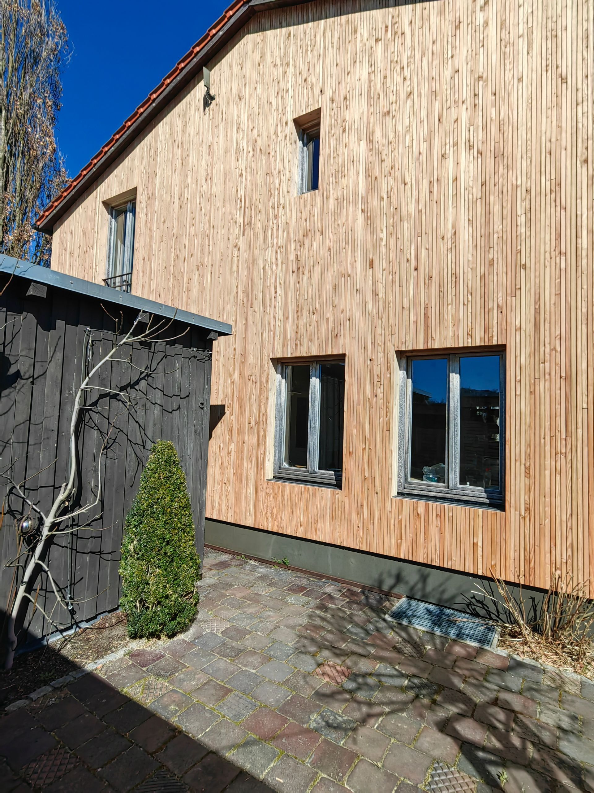 Sanierte Gebäudefront mit vertikaler Holzfassade aus Lärche und klar definierten Fensteranschlüssen - nachhaltiges Fassadendesign von Zimmerei bauwerk singer in Rosenheim