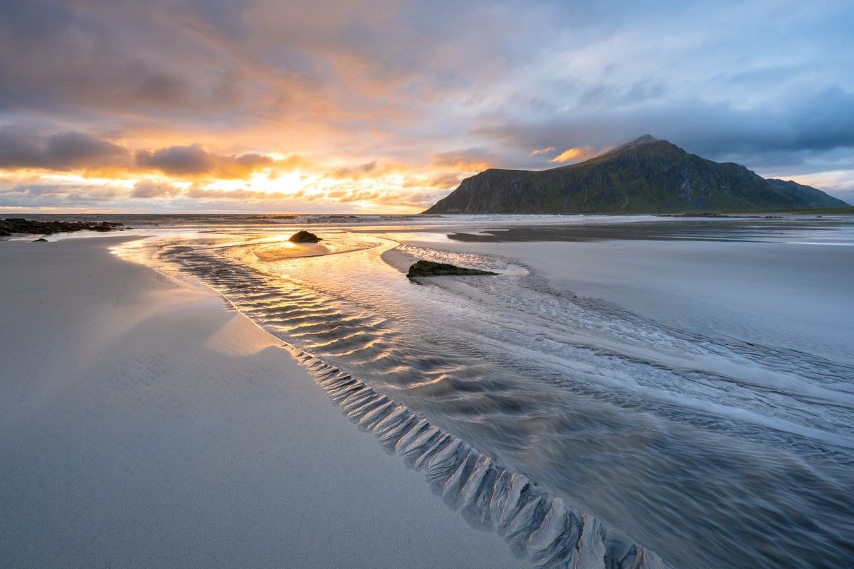 Picture with a colourful sky with a mountain in the background and a beach in the foreground at Skagsandan beach at summer solstice