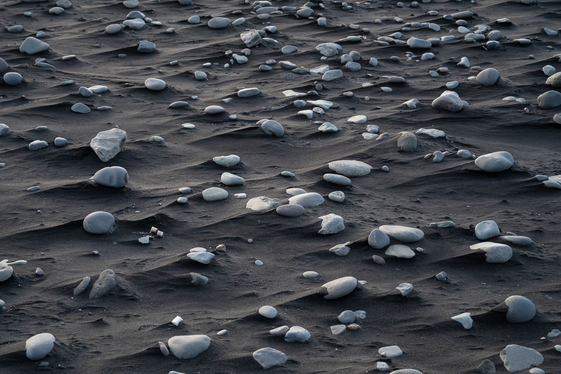 Detailaufnahme mit abstrakten Formen von schwarzem Sand und Steinen aus Island