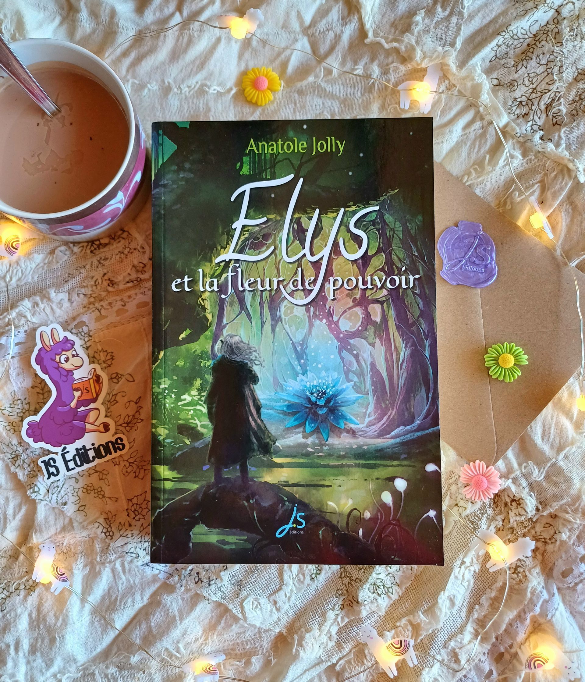 Photo du livre Elys et la fleur de pouvoir dans un décor fait d'un chocolat chaud, d'une enveloppe cachetée et de figurines de fleurs ainsi que d'une guirlande allumée.