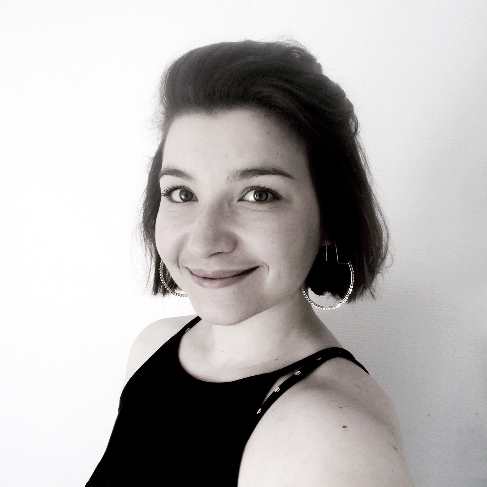 Margot Pilet illustratrice Photo portrait en noir et blanc de Margot Pilet, illustratrice. Elle a des cheveux châtains coupés au carré et porte des créoles. Elle est souriante. Ses yeux semblent foncés.