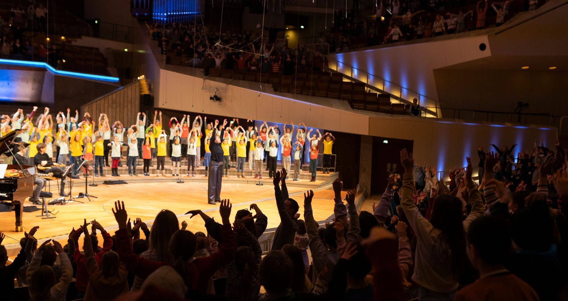 Der Jugendchor sitzend beim Singen mit Simon Halsey vorne stehend als Dirigent.