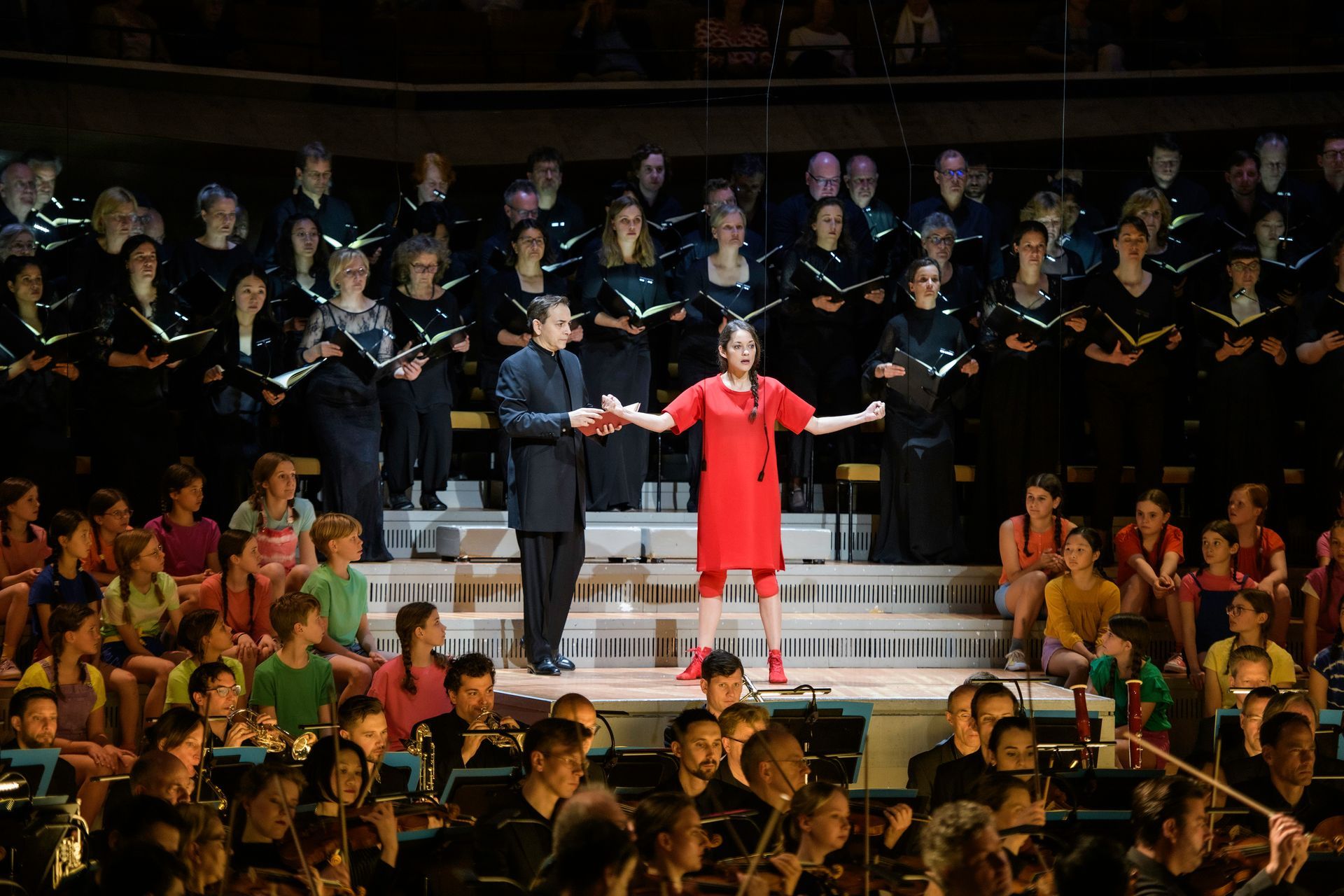 Der Jugendchor sitzend beim Singen mit Simon Halsey vorne stehend als Dirigent.