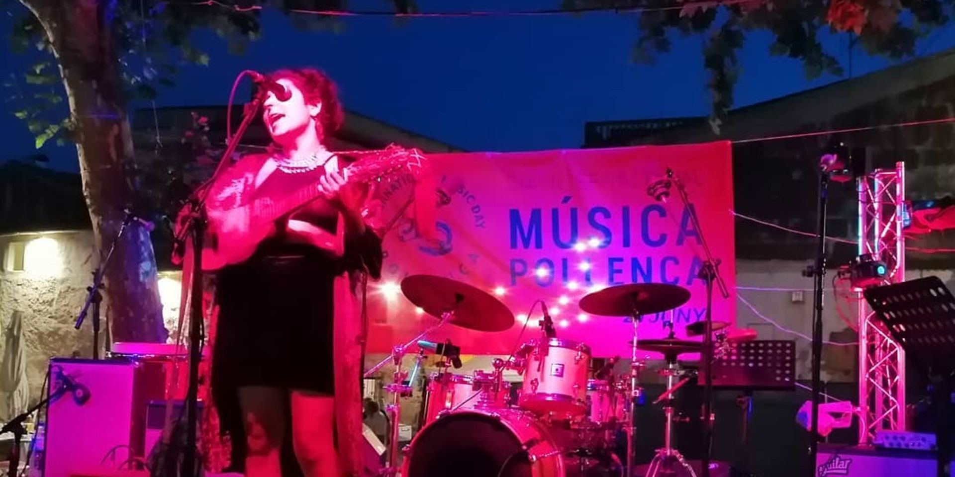 Konzertbühne mit Sängerin mit Gitarre in rotem Scheinwerferlicht am Abend