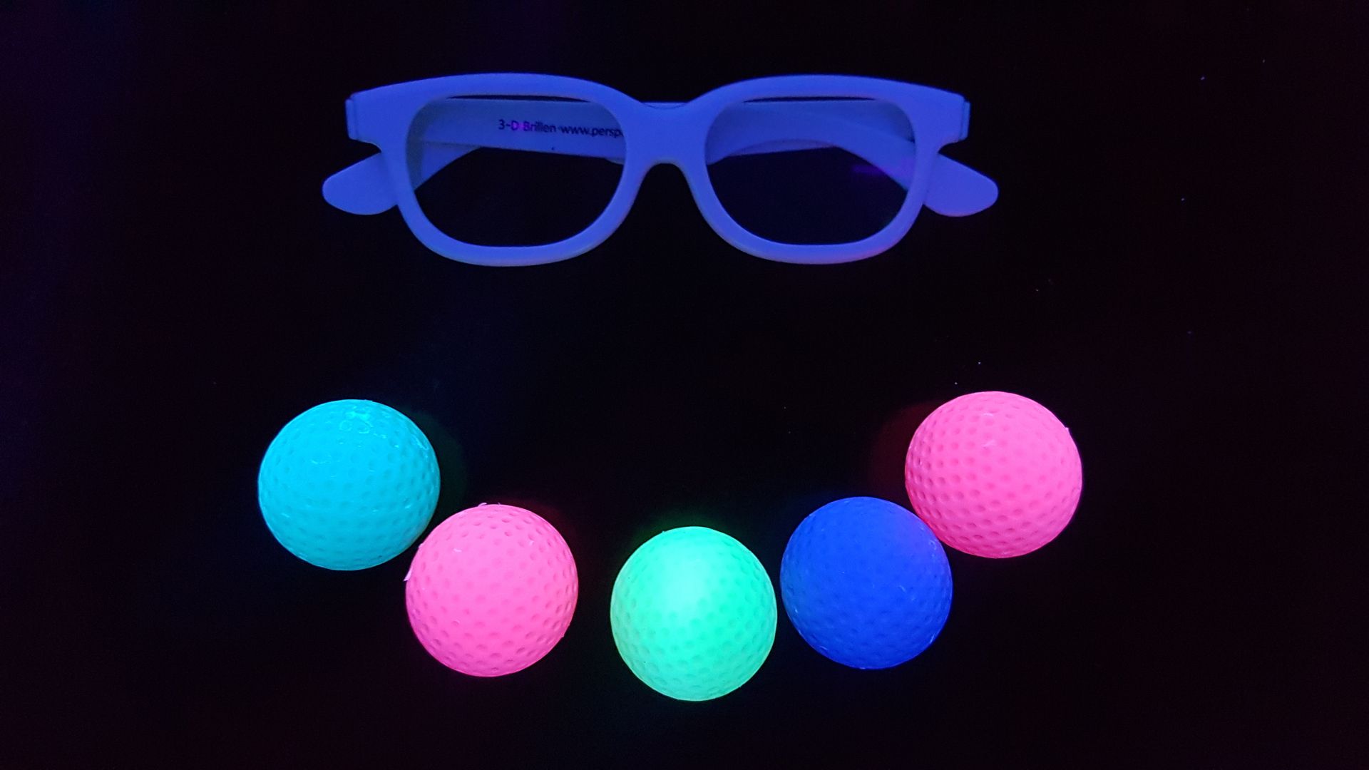 Bild 3D Minigolf-Brille und fünf farbige Minigolf-Bälle vor schwarzem Hintergrund