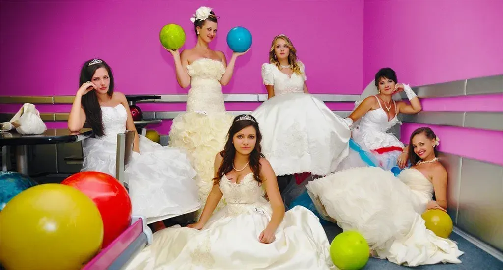 Bild Gruppe von Frauen in Hochzeitskleidern mit Bowlingbällen in einem pinkfarbenen Raum