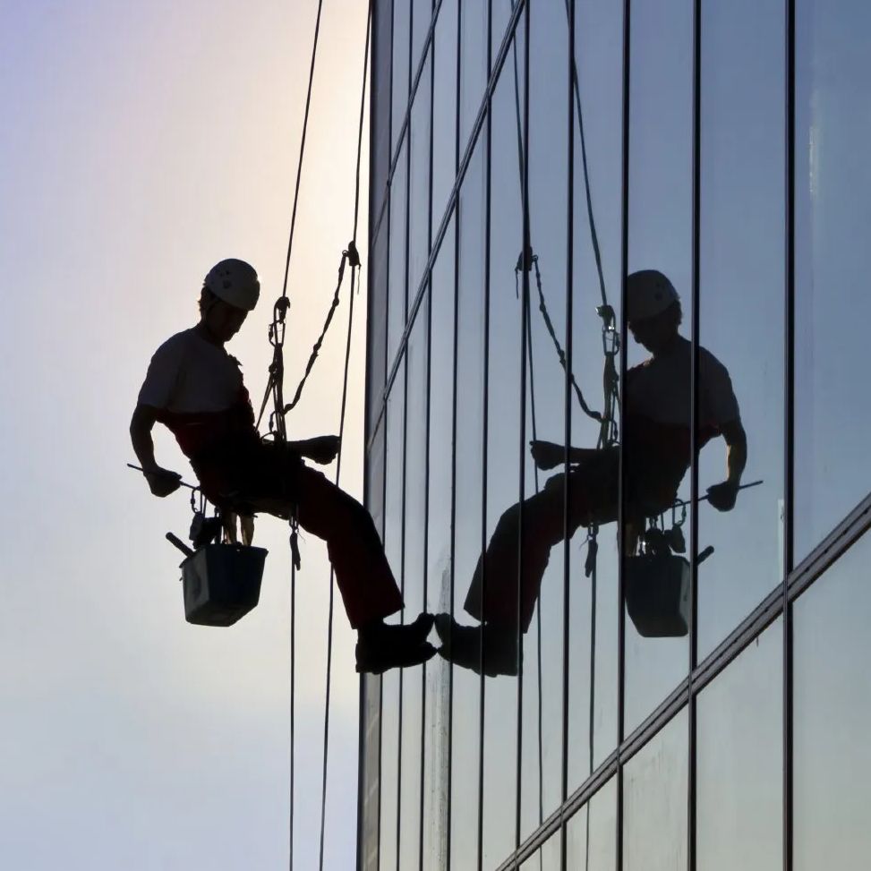 Ein Fensterreiniger der sich mit Sicherheitsausrüstung von einem Hochhaus abseilt und die Fenster reinigt.
