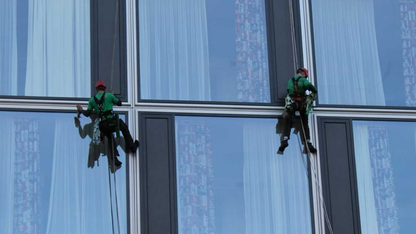 Zwei Fensterreiniger der sich mit Sicherheitsausrüstung von einem Hochhaus abseilt und die Fenster reinigt.