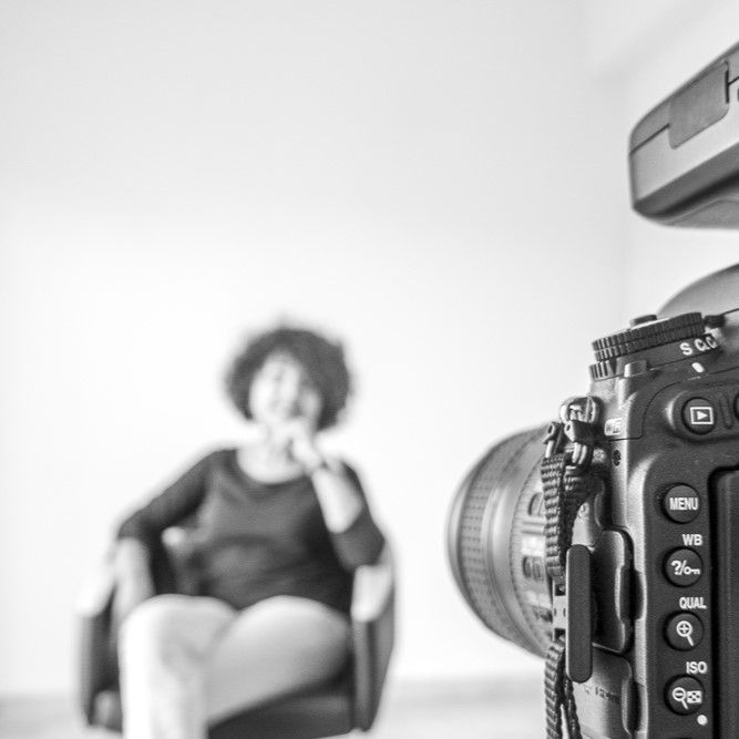 Appareil photo en premier plan, femme assise dans un fauteuil en arrière plan flou.