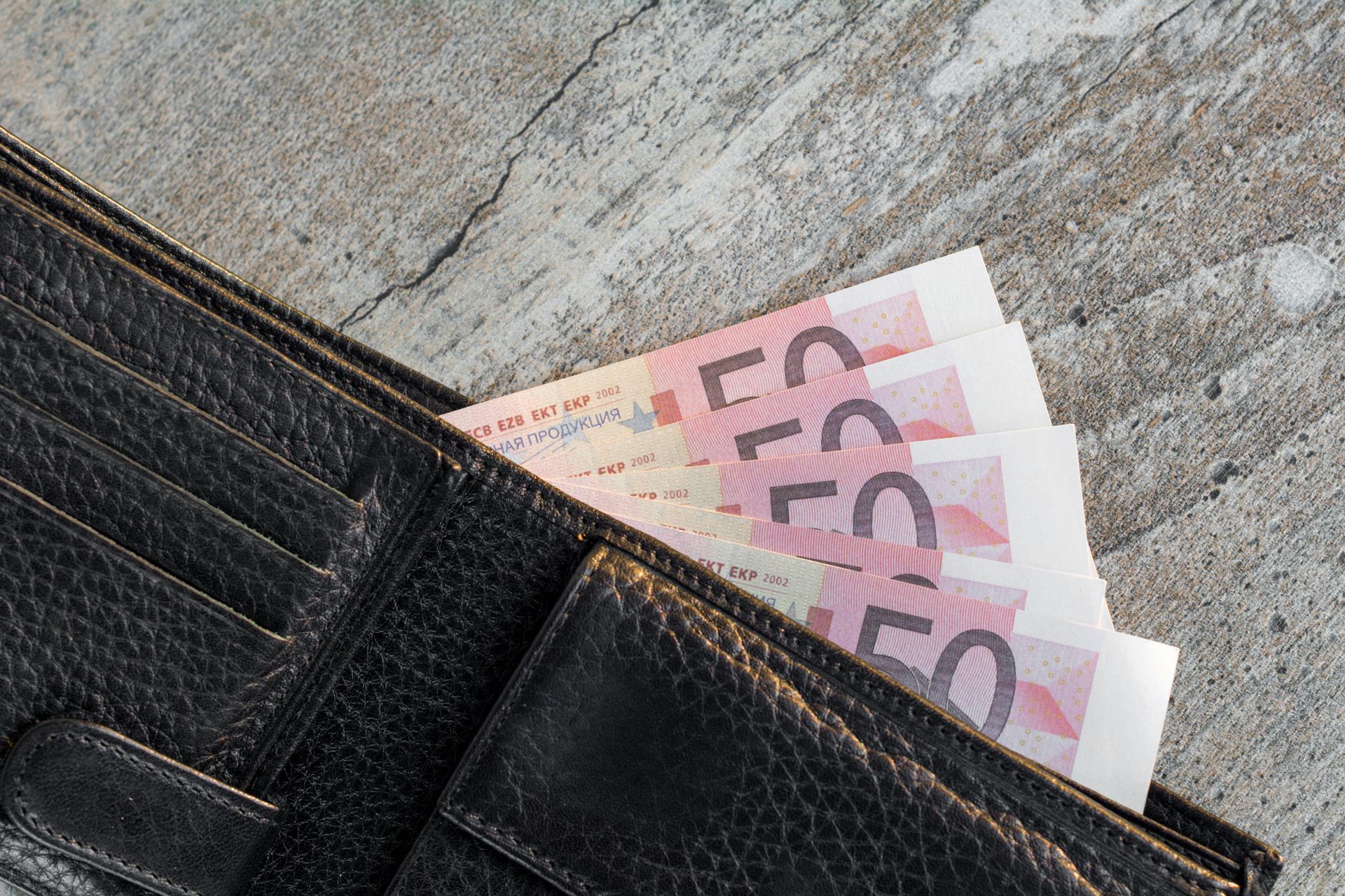 Eine Geldbörse mit mehreren aufgefächerten und rausguckenden 50 Euro Scheinen liegt auf dem Tisch.