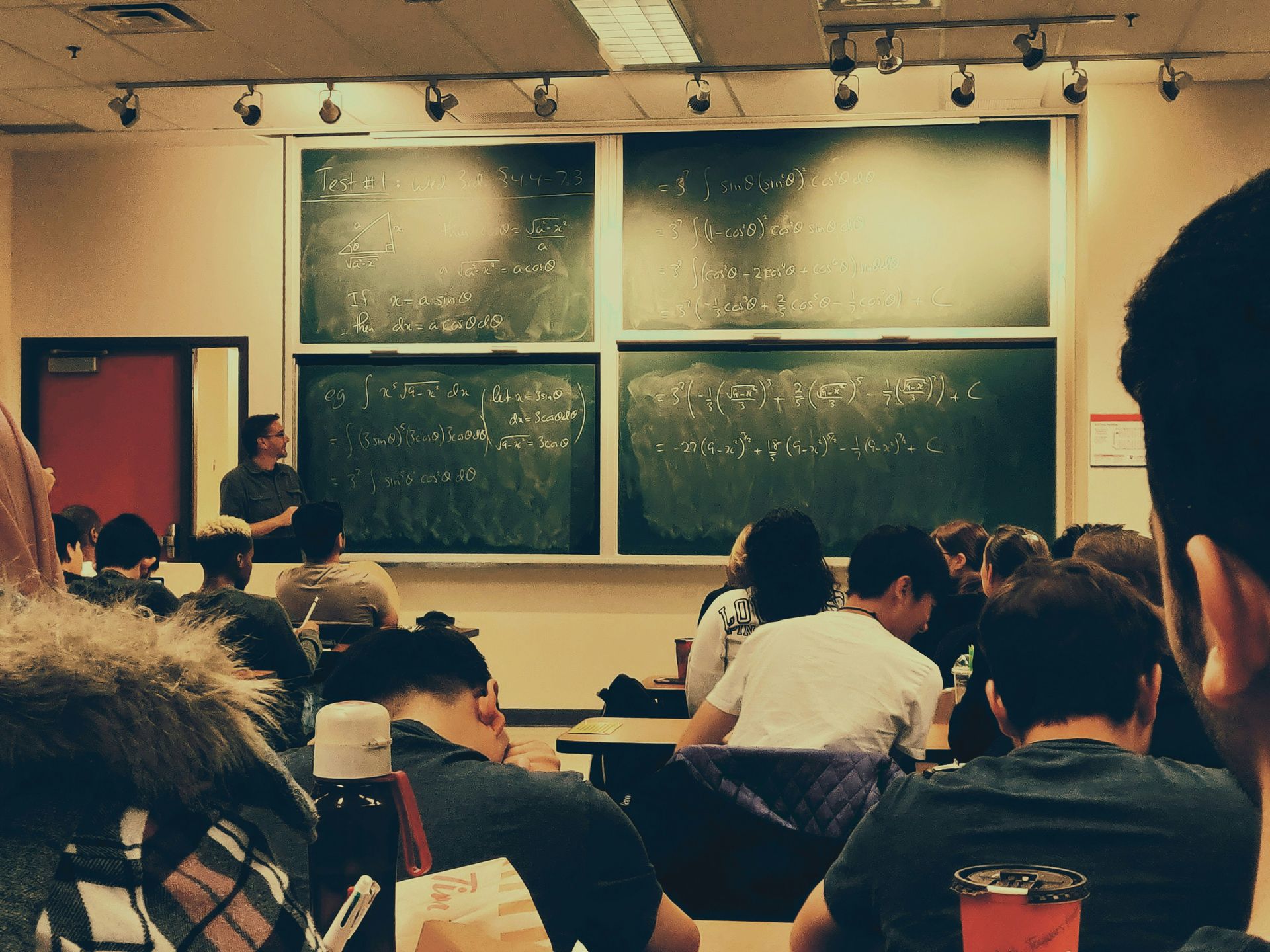 Ein Lehrer, an einer großen Tafel stehend, vor einer Schulklasse.