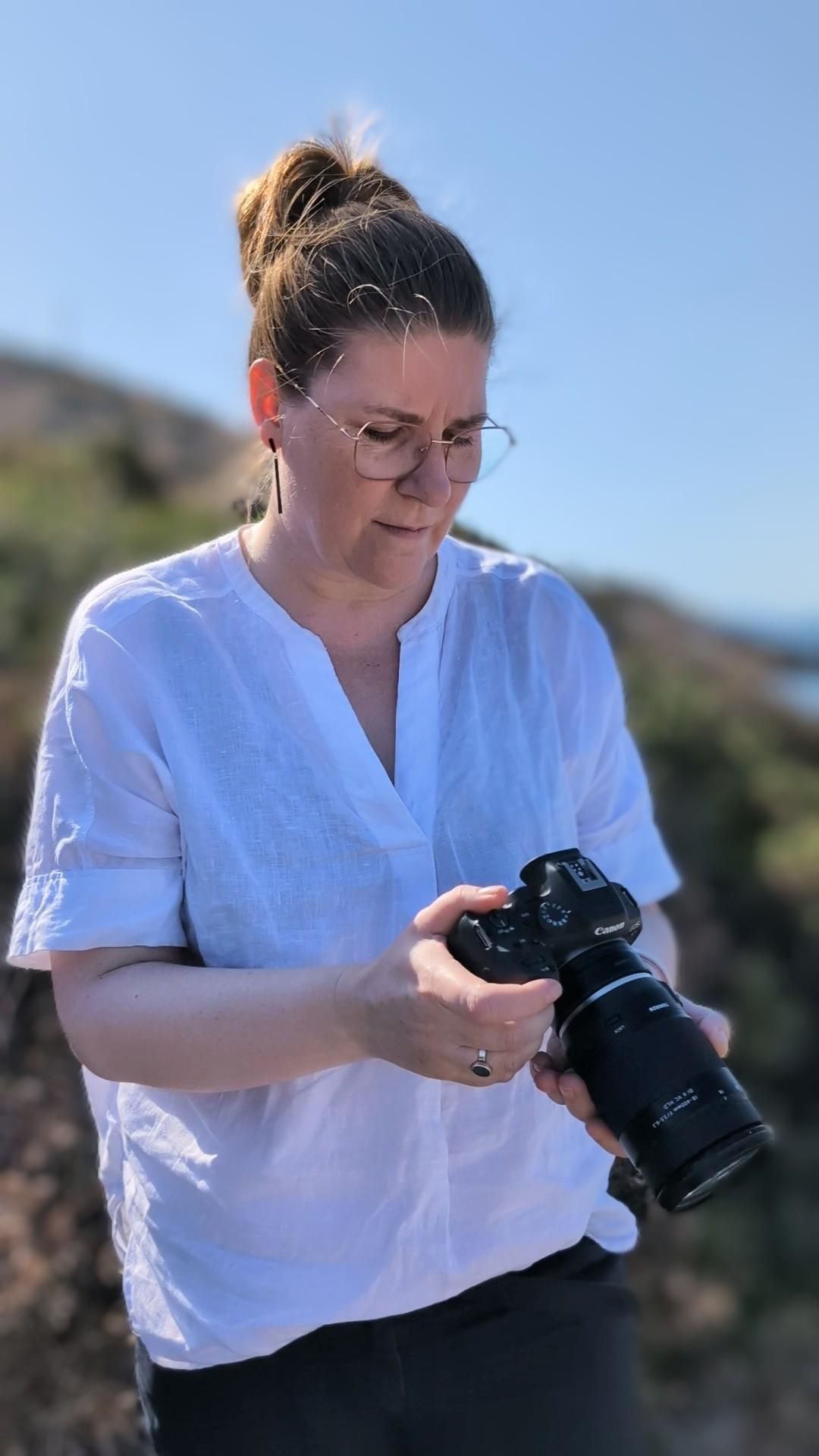 Eine Fotografin in weißer Bluse schaut auf ihre Kamera.
