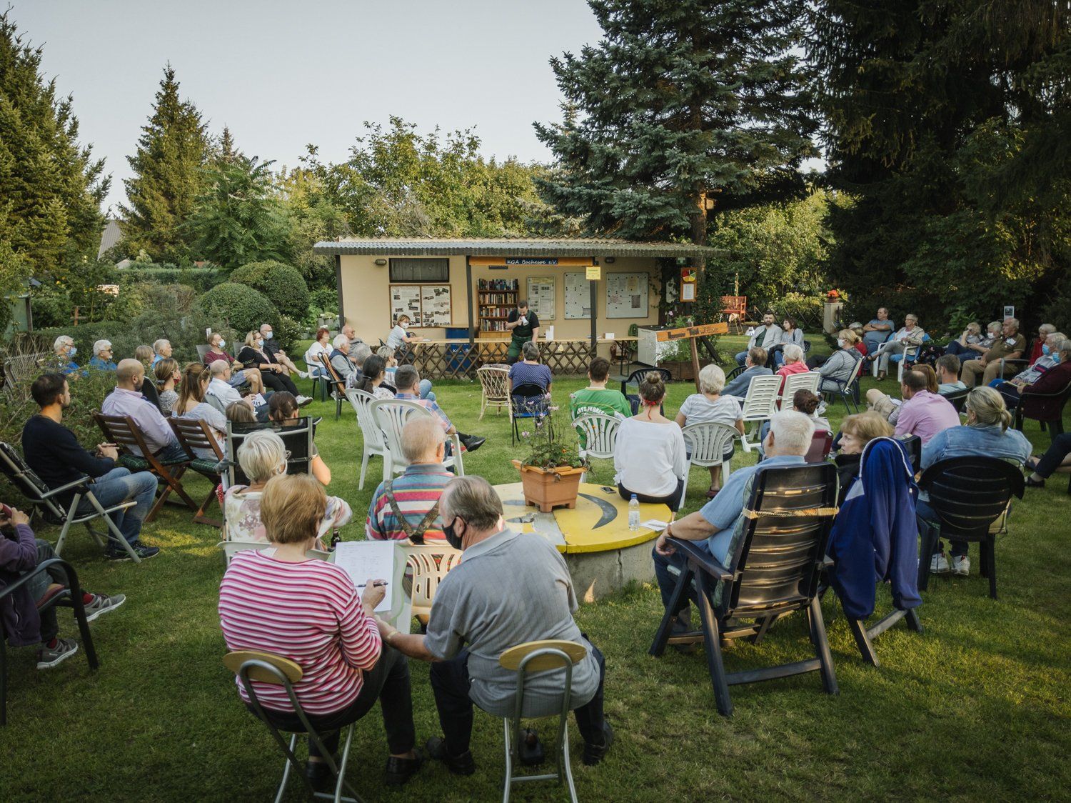 Bild von der Festwiese am Pumpen. Viele Mitglieder sitzen mit dem Rücken zur Kameraaufnahme auf der Wiese auf Stühlen und blicken Richtung Pumpenhaus.