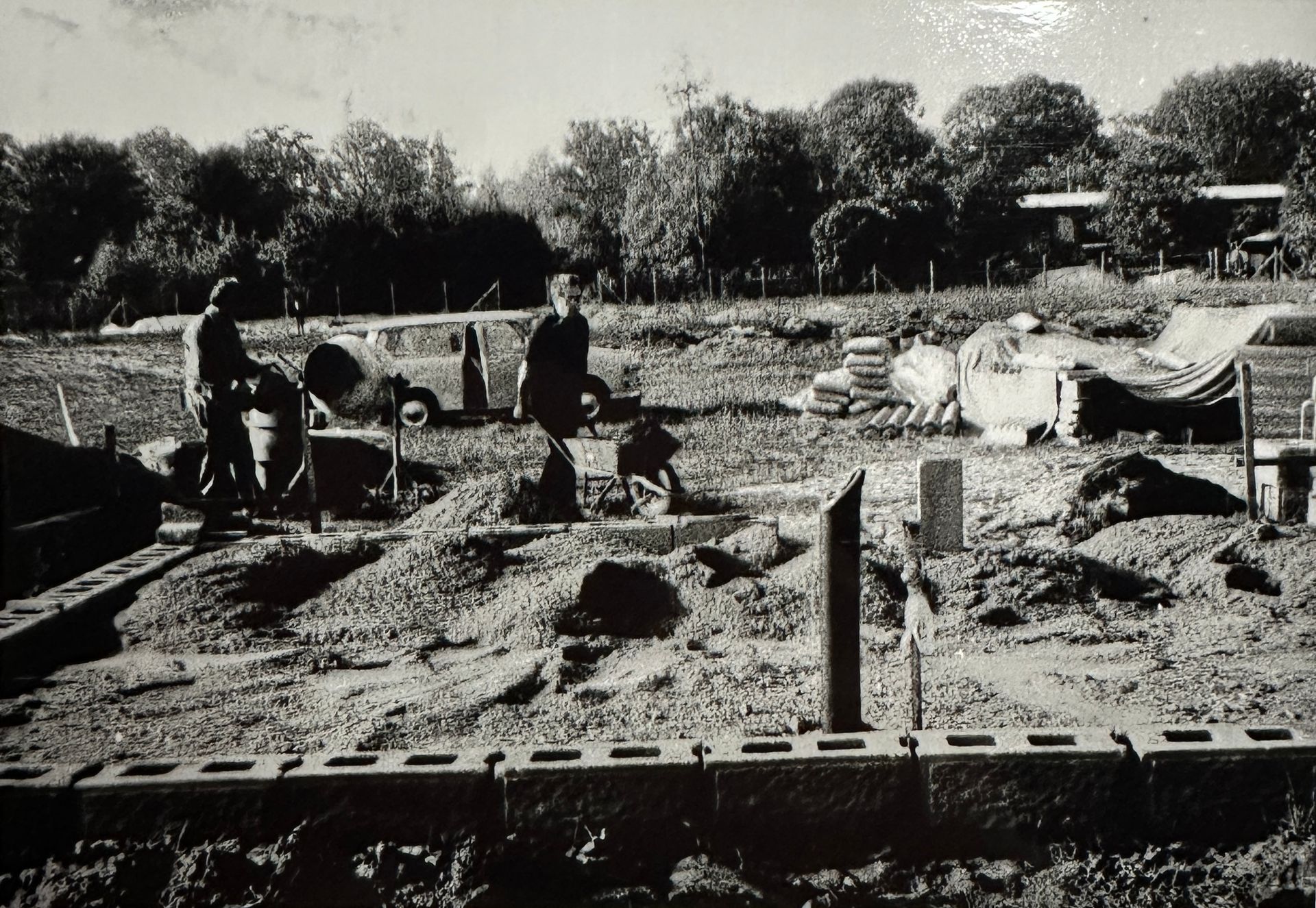 2 Pächter auf der Baustelle. Eine schiebt eine Schubkarre zu einem mit Steinen abgrenzten Rechteck (wahrscheinlich Fundament für Laube)