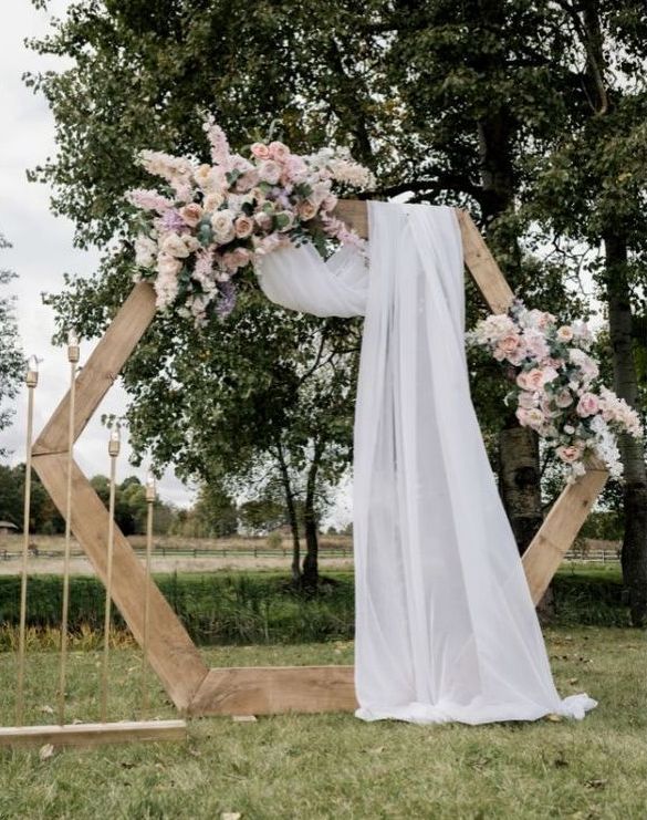 Wunderschön dekorierter Traubogen aus Holz mit Blumen und Tüchern in pastellrosa. Im Hintergund zeicnet sich ein Tal ab.