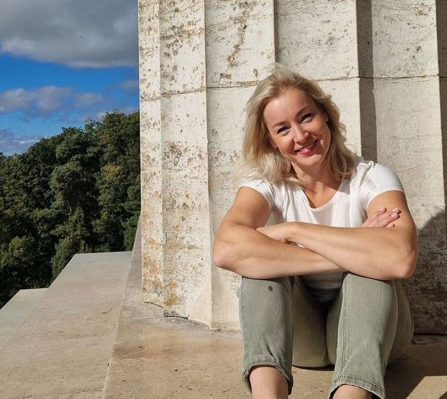 Lucile, die vor eine Säule der Walhalla sitzt, Arme sind locker verschränkt. Das Bild hat eine sehr freundliche Stimmung.