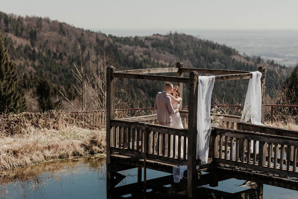 Brautpaar in inniger Umarmung auf einem dekorierten Holzsteg, der ins Wasser ragt.