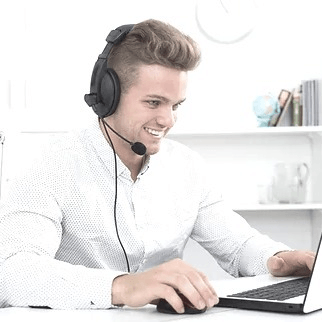 Junger Mann mit mittelbraunen Haaren, zurückgekämmt, weißes Hemd, mit Telefonheadset.  Er sitzt an einem Schreibtisch, vor sich ein Laptop. Hintergrund weiß mit weißem Bücherregal.