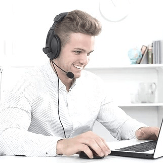 Telefonberatung Junger Mann mit mittelbraunen Haaren, zurückgekämmt, weißes Hemd, mit Telefonheadset. Er sitzt an einem Schreibtisch, vor sich ein Laptop. Hintergrund weiß mit weißem Bücherregal.