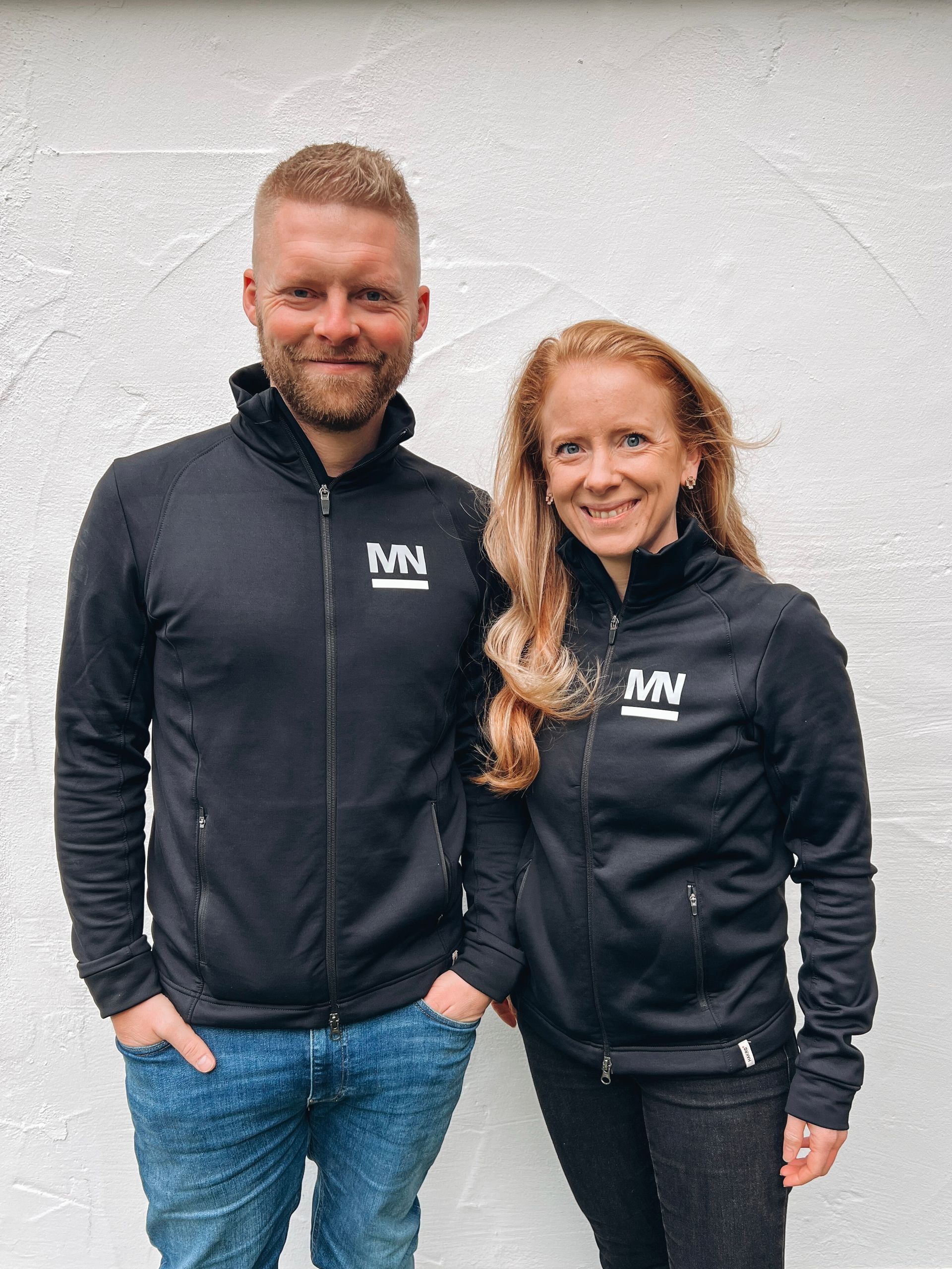 Marcel und Miriam Inhaber des EMS Studios stehen vor einer weißen Wand und lachen