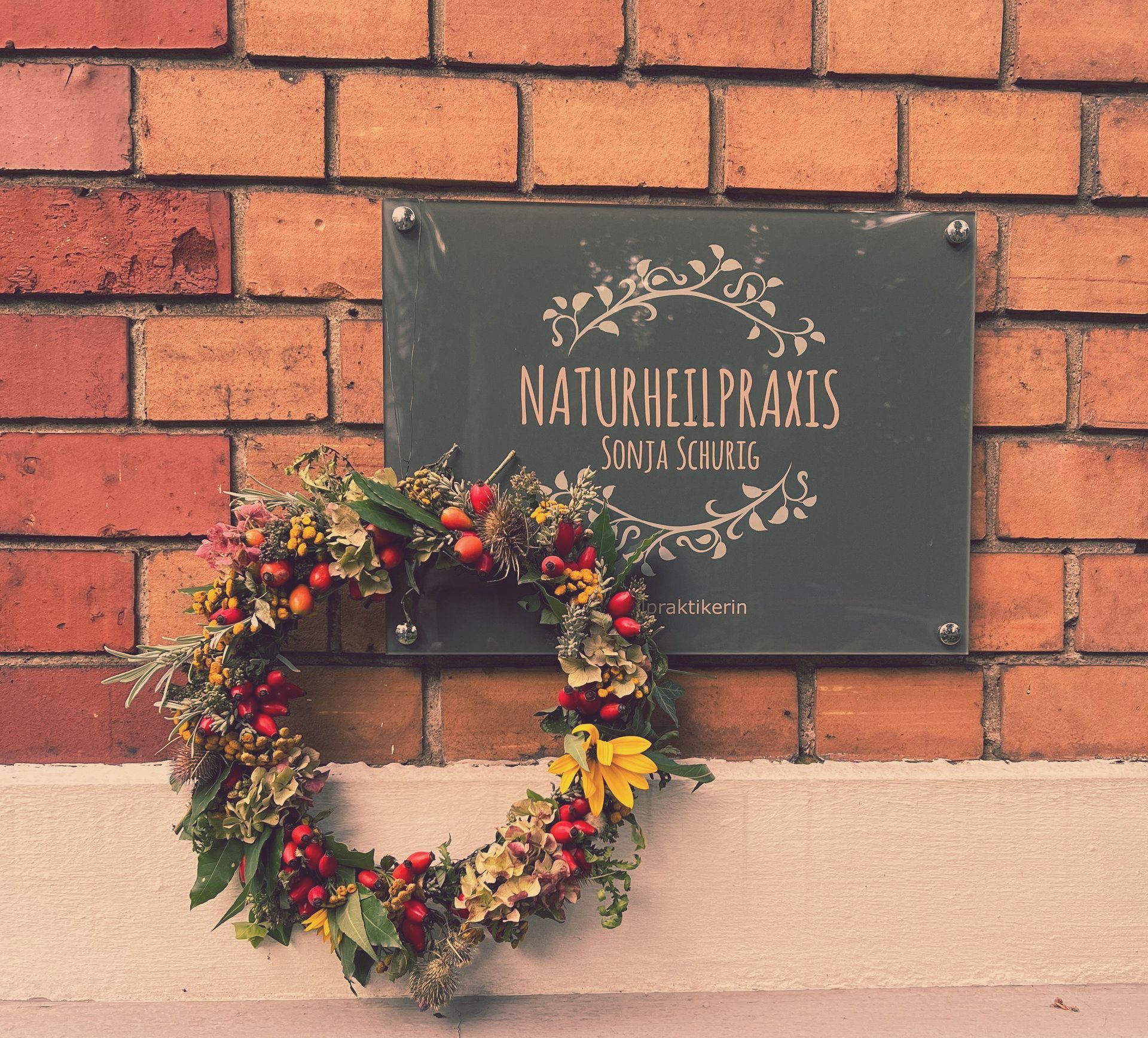 Praxisschild mit Blumenkranz