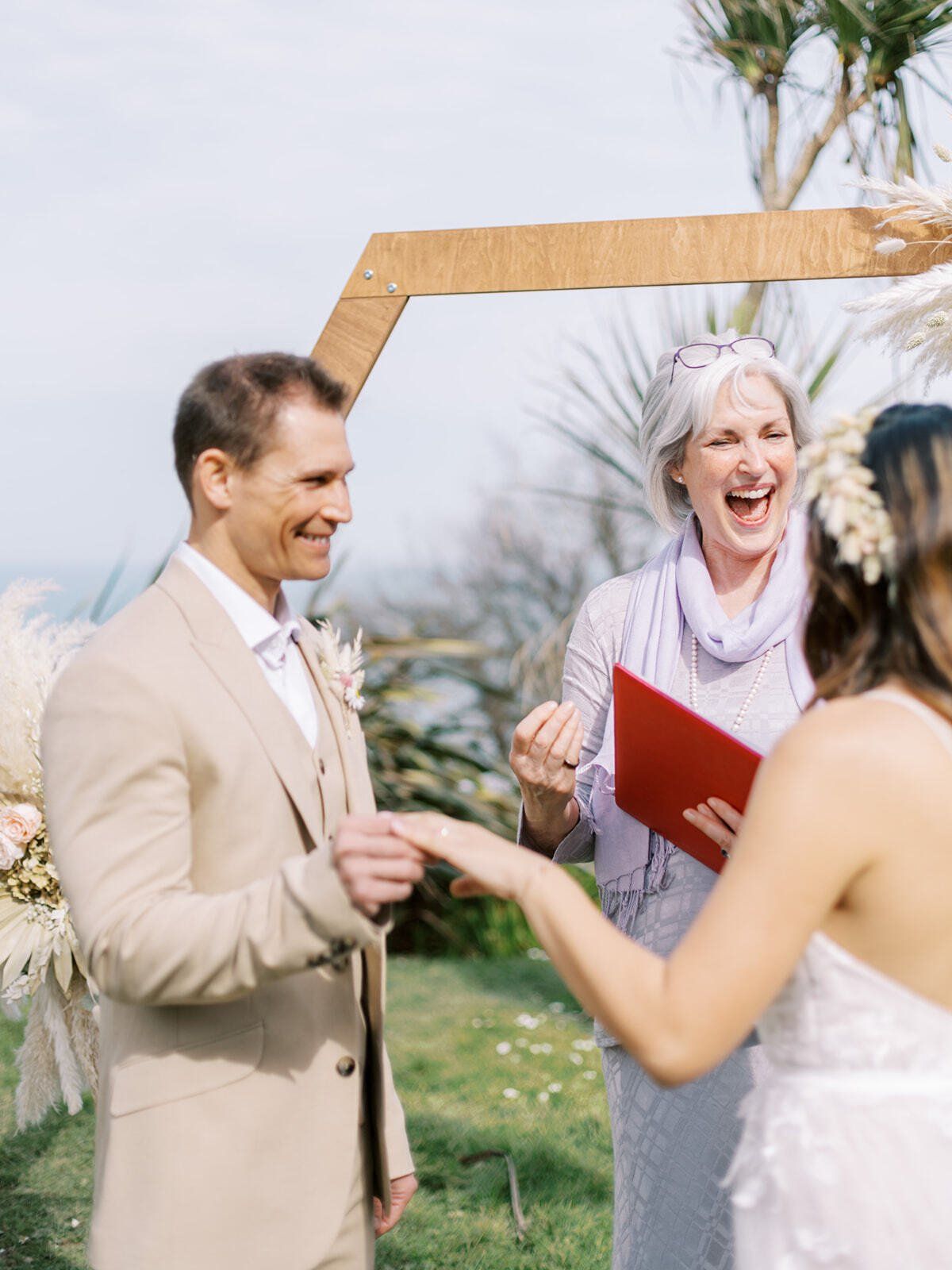 bride and Sara Price Celebrant laughing whilst groom watches and smiles during their ceremony by the sea.