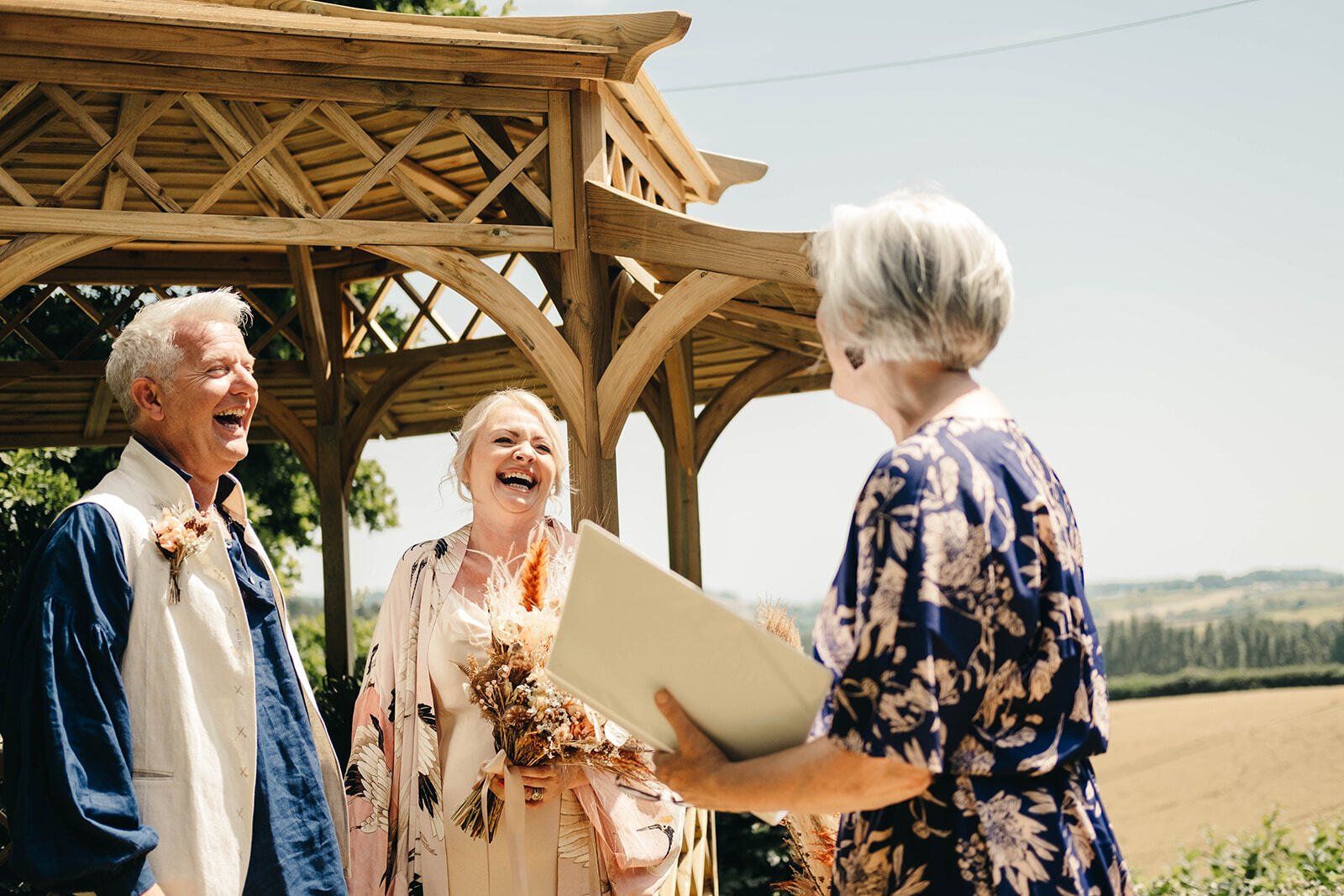 Bride and groom laughing at something Sara Price Celebrant said during their outdoor vow renewal ceremony.