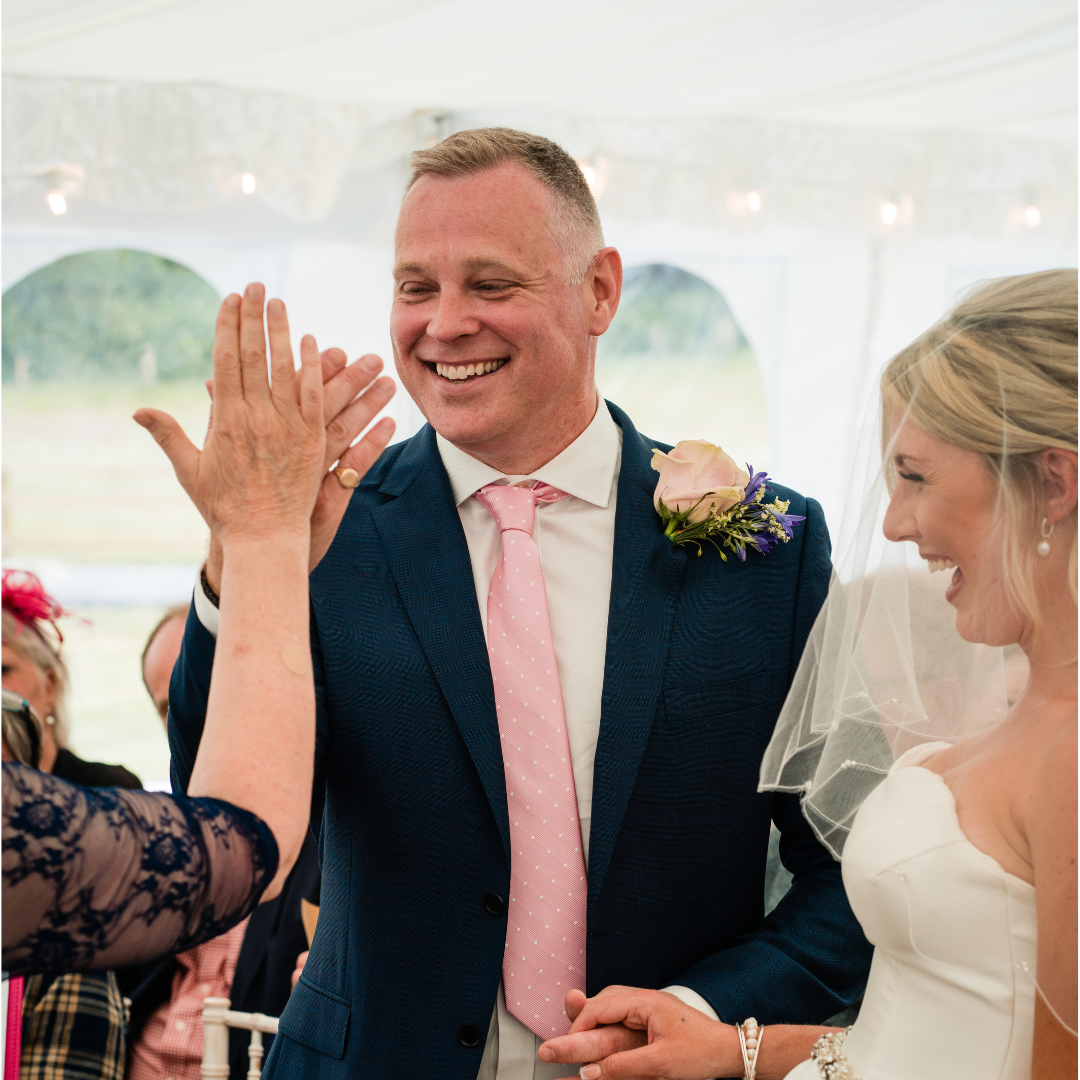 Groom high fives Sara Price Celebrant whilst bride is laughing as she watches them during their wedding ceremony.
